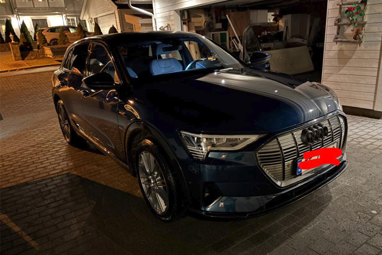 En mørk blå Audi e-tron parkert i en opplyst innkjørsel om natten.