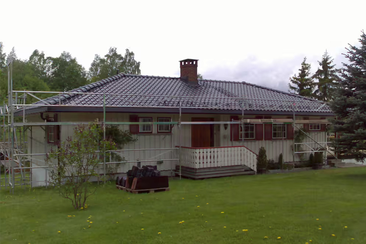 En enebolig med takrenovering, plassert i en grønn hage med trær og gress.