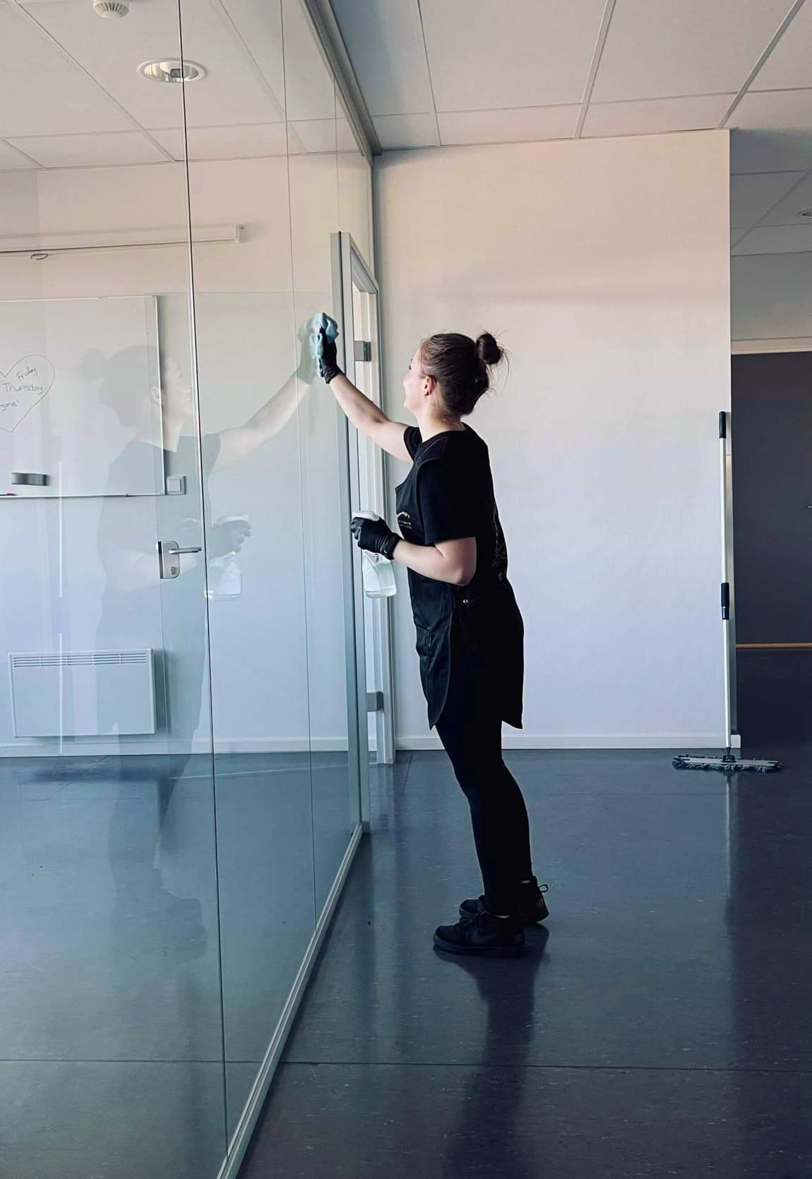 En kvinne rengjør et glassvindu i et moderne kontorlandskap.
