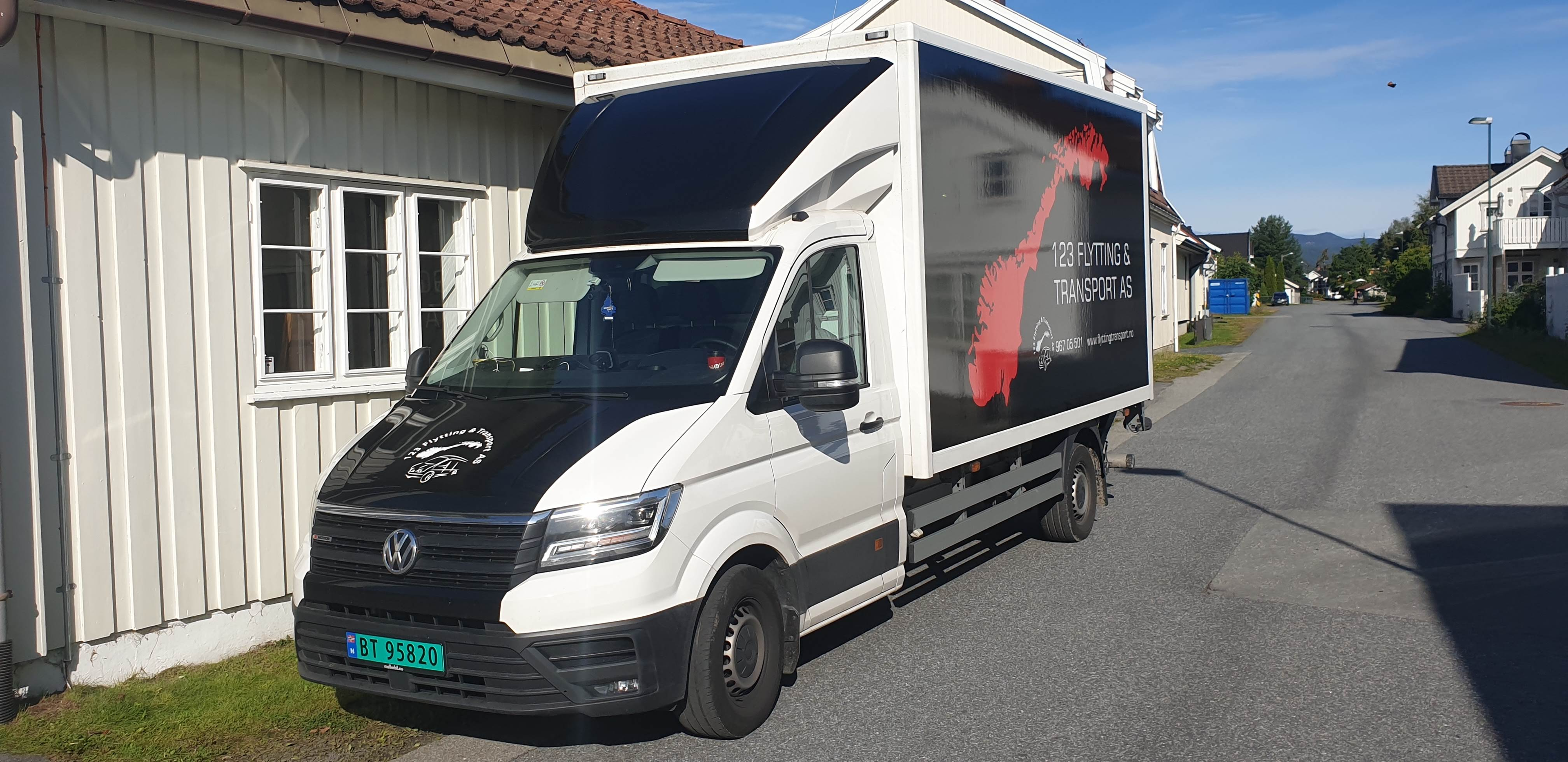 En hvit lastebil med svart tak står parkert ved en bygning i et boligområde.