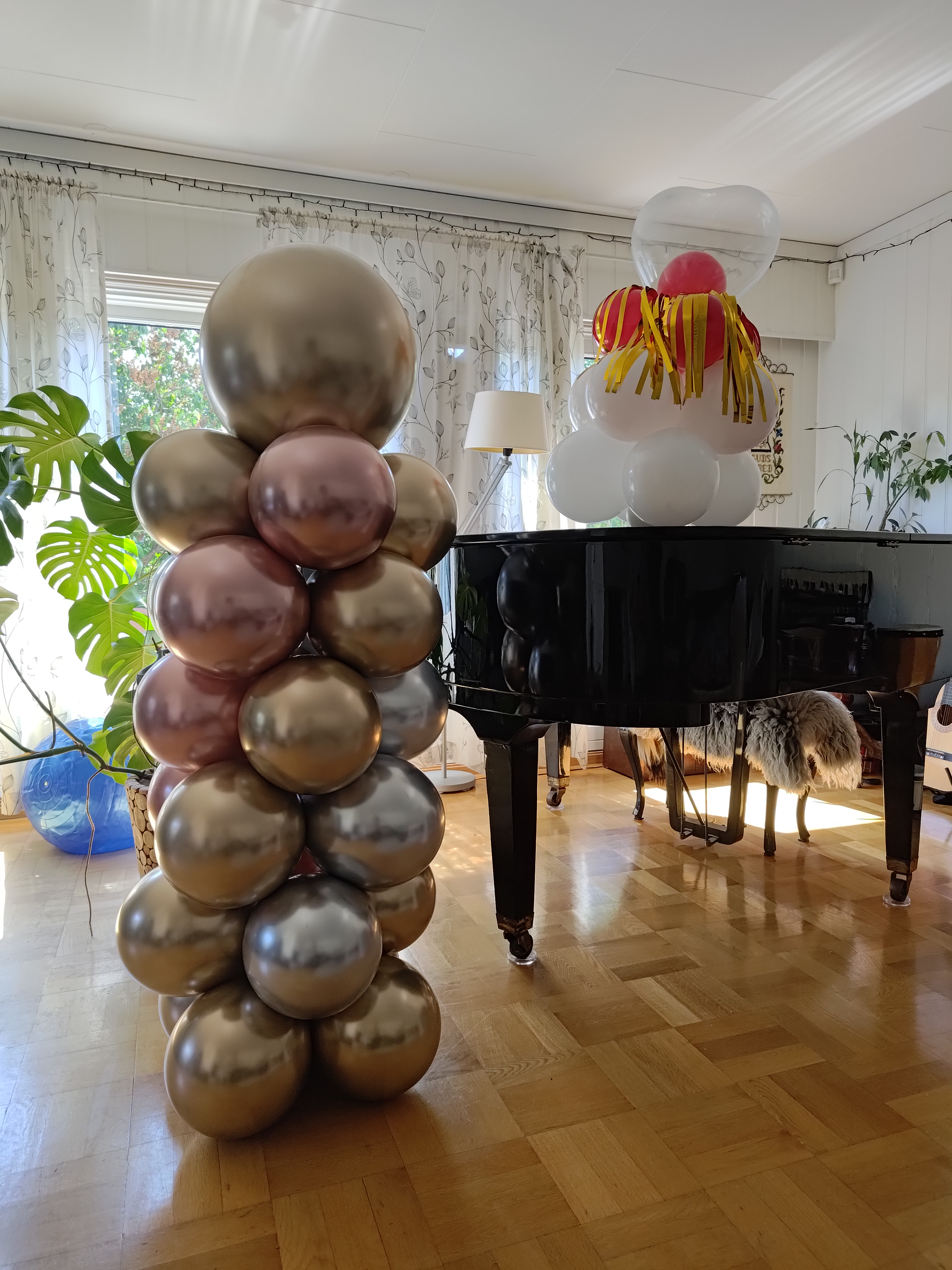 Fargerike ballonger stablet ved et piano i stue med planter i bakgrunnen.