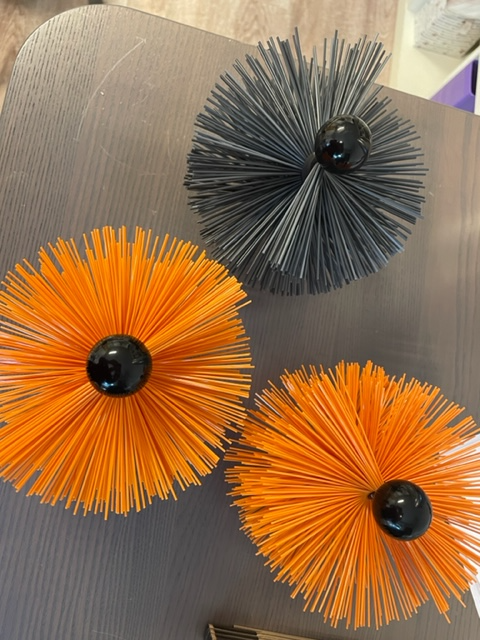 Tre dekorative blomster laget av fargerike plaststrå, i oransje og svart, med en svart kule i midten.