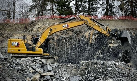 Gravemaskin i arbeid på en steinbrudd, med gult CAT-merke og steinmateriale rundt.