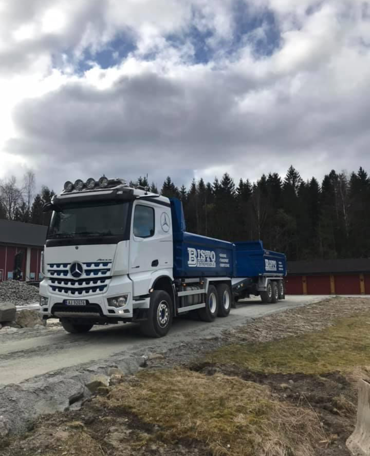 En stor lastebil fra Mercedes-Benz med tilhenger, parkert på en grusvei med skog i bakgrunnen.