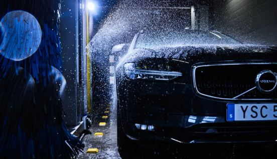 En svart Volvo bil som blir vasket i en bilvask med vannsprut og børster.