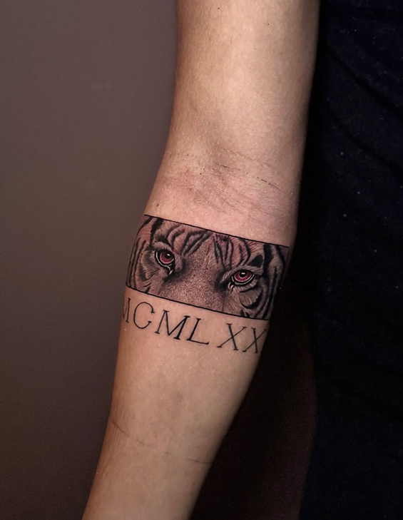 Tatovering av en tiger med intense øyne og romerske tall "MCMXLXX" på en arm.