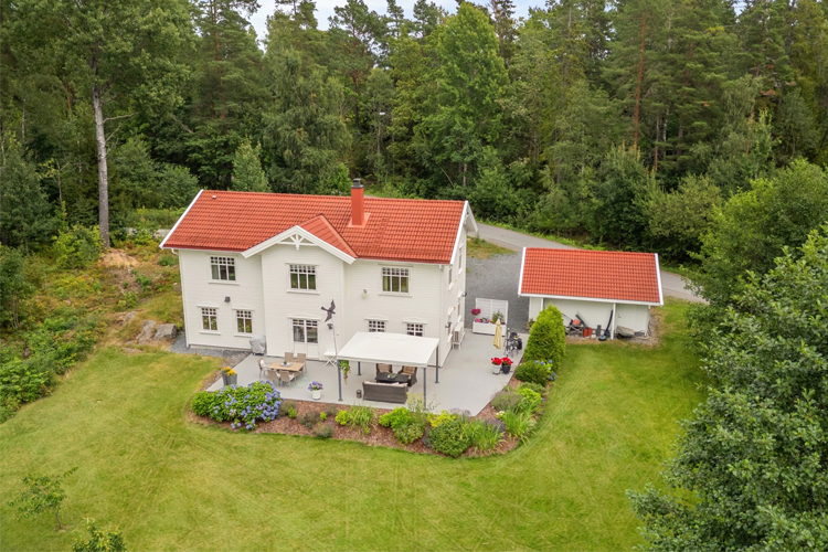En stor, hvit enebolig med rød takstein, omringet av grønt landskap og trær.