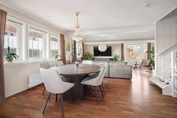Moderne stue med spisebord, stoler, sofa og store vinduer som slipper inn naturlig lys.