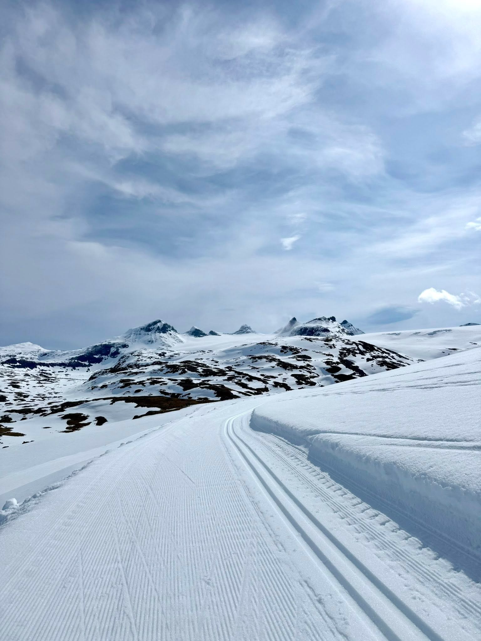 En snøfylt langrennsløype som snirkler seg gjennom fjellandskapet under en lys himmel.