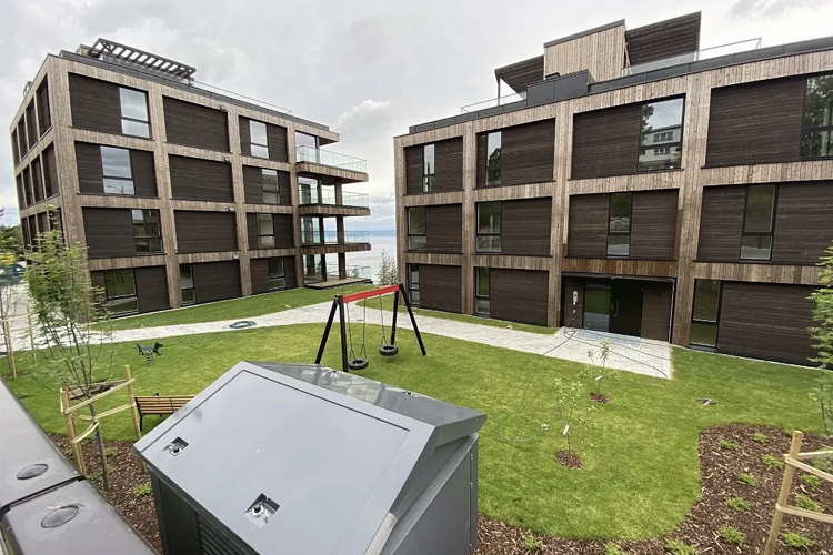 Moderne leilighetsbygg med lekeplass og grøntområde, beliggende ved vannet.