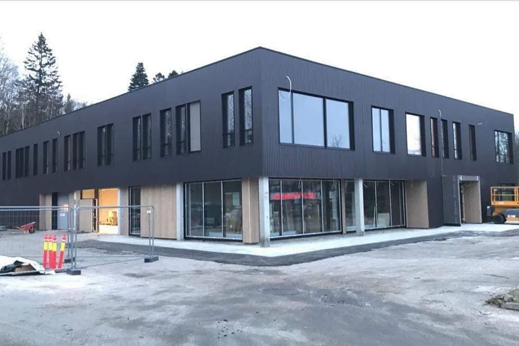 Moderne bygning med mørk fasade og store vinduer, under konstruksjon i et urbant område.