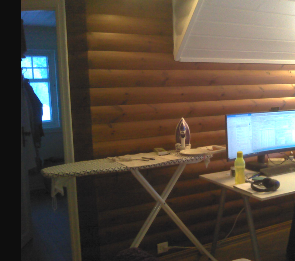 Et strykebrett med et strykejern og en datamaskin står mot en vegg av trepanel i et rom.