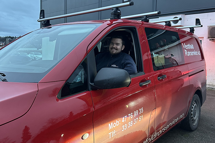 En smilende mann sitter i førersetet på en rød varebil med takstativ.
