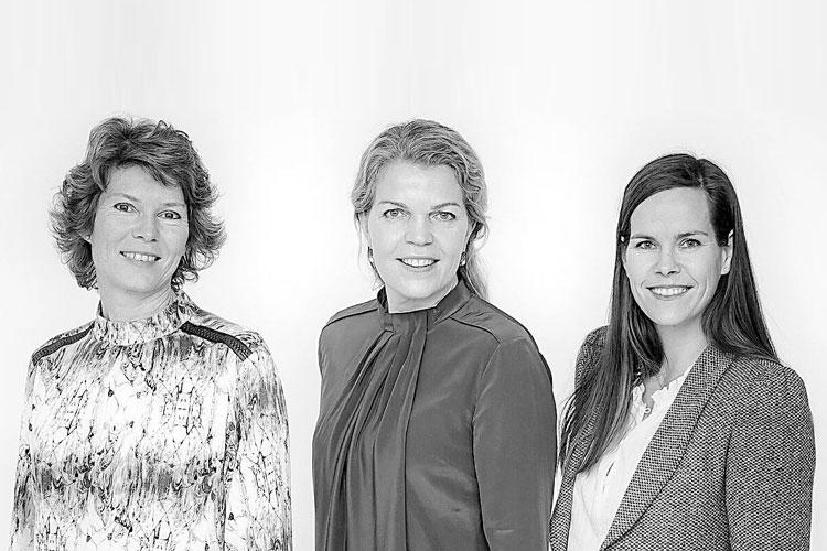 Tre kvinner står sammen foran en lys bakgrunn, smilende og kledd i profesjonelle klær.