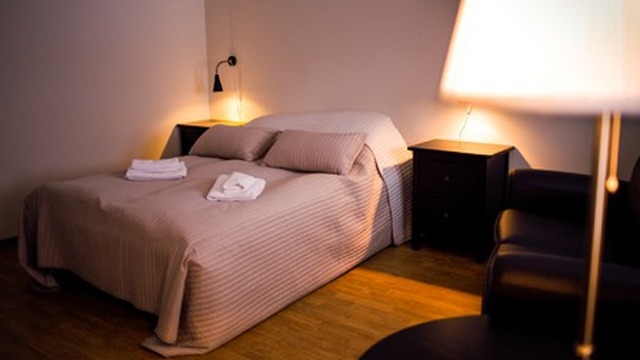 Et koselig soverom med en dobbeltseng, sengetøy, nattbord og en lampe i dempet belysning.