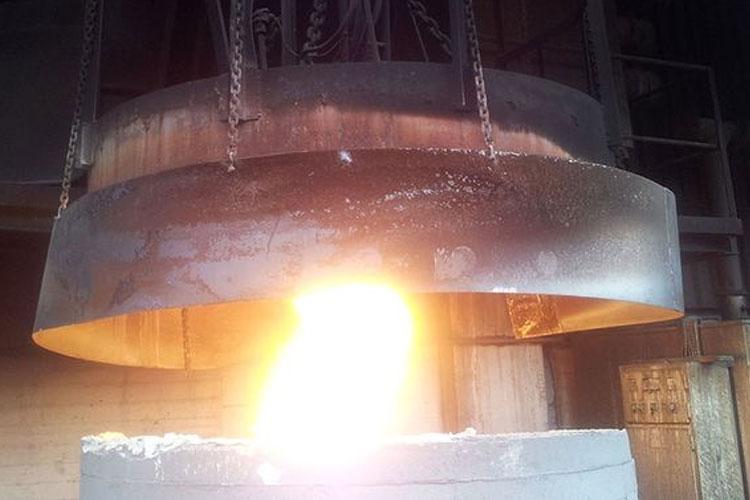 En smeltedigel med glødende metall som strømmer ut, hengende fra taket i en smelteovn.