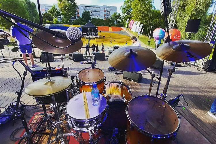 Utsikt fra trommesettet med mikrofon og scene i bakgrunnen, klar for konsert med publikum og fargerike ballonger.