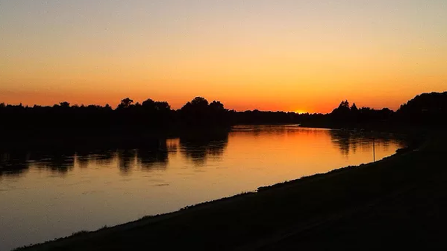 Solnedgang over elven med speilbilde av trær og himmel i varme farger.