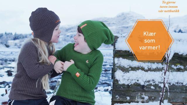 To barn iført varme, strikkede klær, smilende og leende i vinterlandskap. Tekst: "Klær som varmer!"