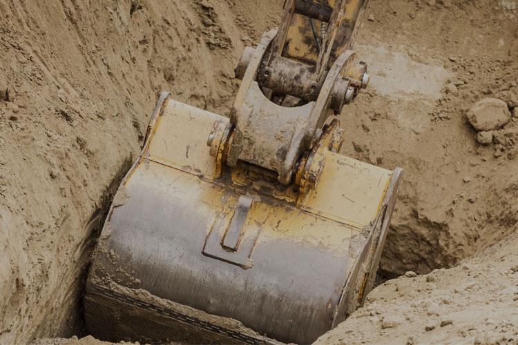 Gravemaskin som graver i sandjord med en stor skuffe i fokus.