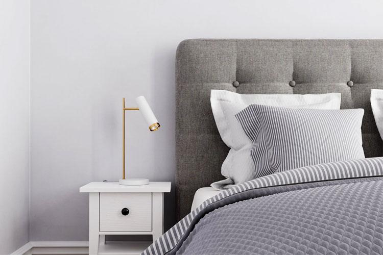 Soverom med grå sengesett, hvite puter, og en moderne nattbordlampe ved siden av sengen.