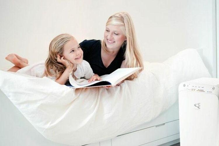 Mor og datter ligger på sengen og leser en bok sammen, med et lyst rom i bakgrunnen.