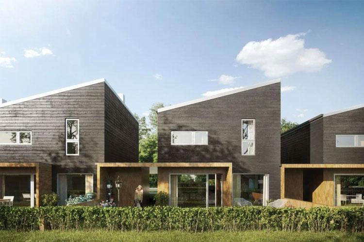 Moderne hus med skråtak og treverk, omgitt av grønt gress og busker under en klar blå himmel.
