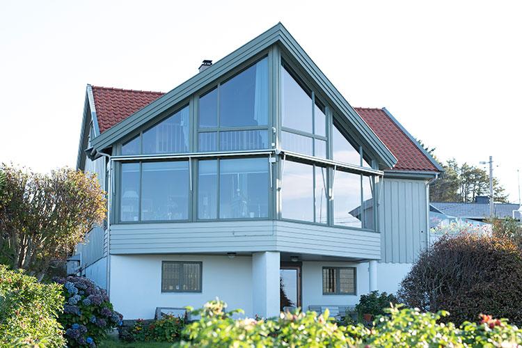 Moderne hus med store vinduer og skråtak, omgitt av hage og grøntområder.