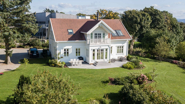 En vakker, hvit enebolig med rød takstein, omringet av grønt gress og hageplanter.