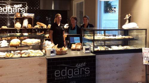 Tre ansatte står foran disken i Edgars bakeri, med ferske brød og bakverk synlige i glassmontrene.