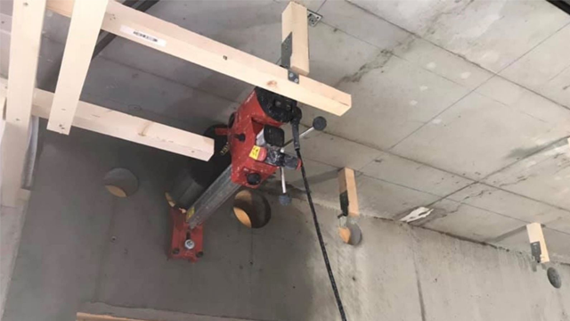 En rød heisinstallasjon festet til taket med treplanker og betongvegger, med synlige hull i betongen.
