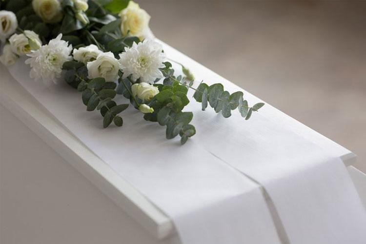 En hvit kiste dekorert med blomster og grønt, inkludert roser og eukalyptus.