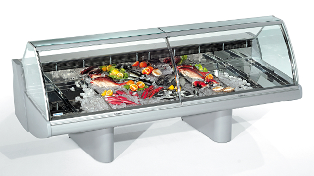 Fiskedisplay med is, fersk fisk og grønnsaker, i en moderne kjøledisk med glasslokk.