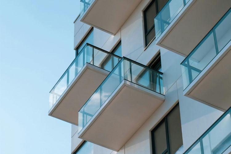 Moderne leilighetsbygg med glassbalkonger og blå himmel i bakgrunnen.