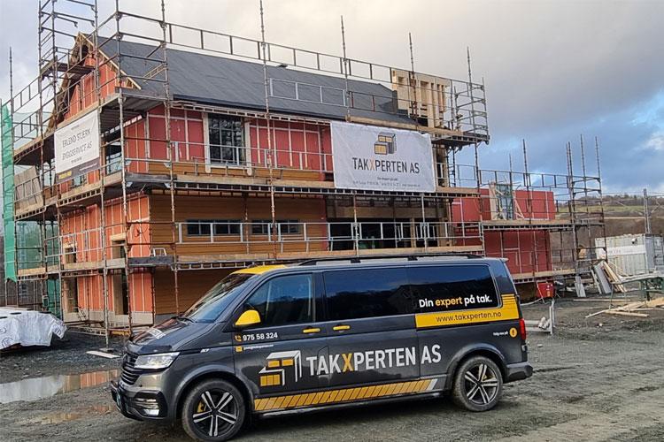 En varebil fra Takk Experten AS står foran en byggeplass med et hus under oppføring og stillas rundt.