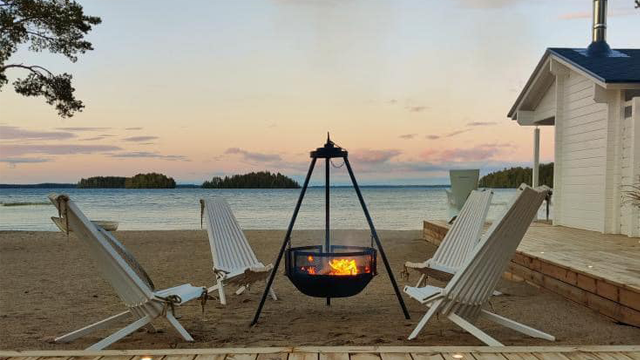 Koselig strand med en bålplass, tre hvite stoler og en vakker solnedgang over havet.