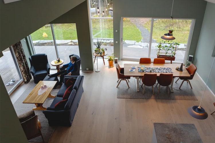 Moderne stue med store vinduer, spisebord, sofaer og en person som sitter i en stol.