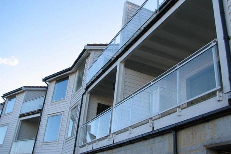 Moderne leiligheter med balkonger og glassrekkverk under en klar blå himmel.