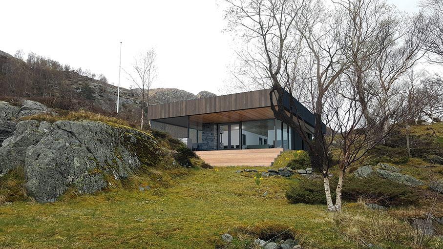 Moderne hus med store vinduer, plassert mellom steiner og trær i et naturskjønt landskap.