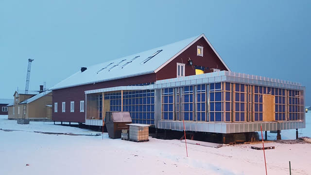 Rødt hus med moderne glassutvidelse, dekket av snø, i skumringen.