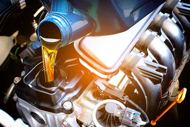 Olje helles i motoren fra en blå kanne, med motorens deler synlige i bakgrunnen.