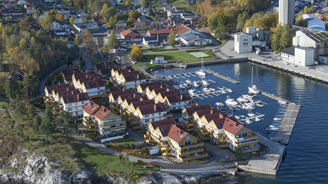 Utsikt over en marina med båter og moderne leiligheter i høstfarger.