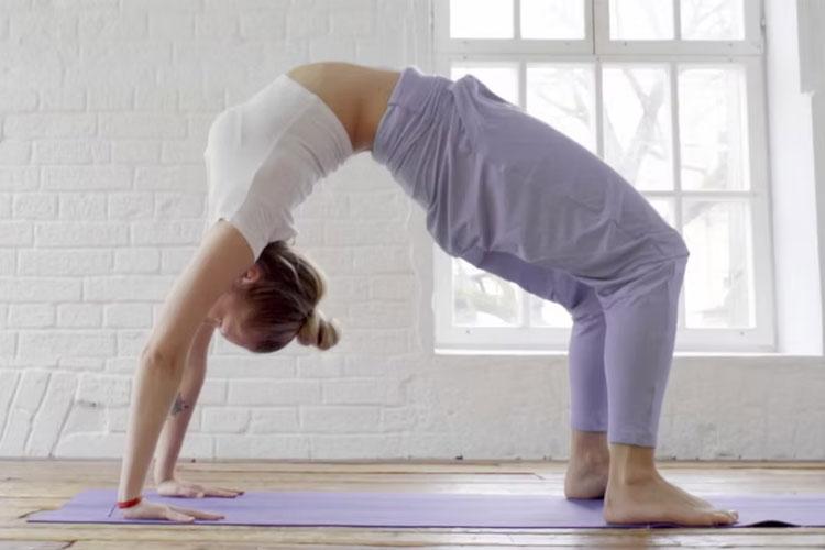 En kvinne utfører yoga i en bakoverbøyning på en yogamatte i et lyst rom.