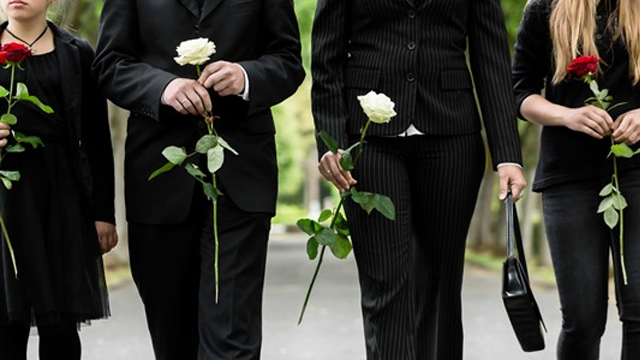 Fire personer i svart antrekk holder roser mens de går på en sti i en park.