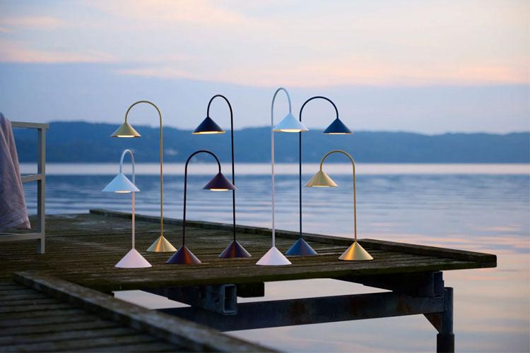 Fargerike lamper med buede stenger står på en brygge ved vannet i solnedgang.