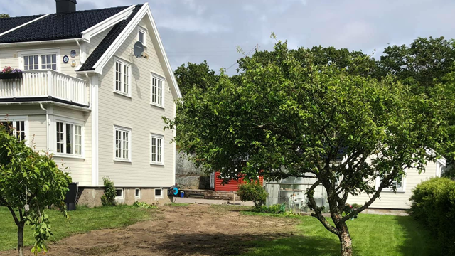 En lys, moderne enebolig med hage og et epletre, omgitt av grønt gress og trær.