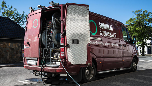 Rød servicebil med åpen bakdør, utstyr for rengjøring synlig, parkert på gaten.