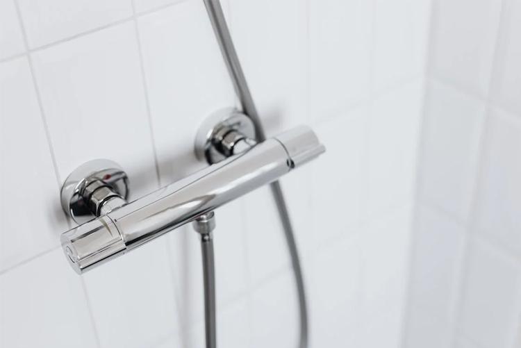 Dusjarmatur i rustfritt stål på en hvit flisvegg.