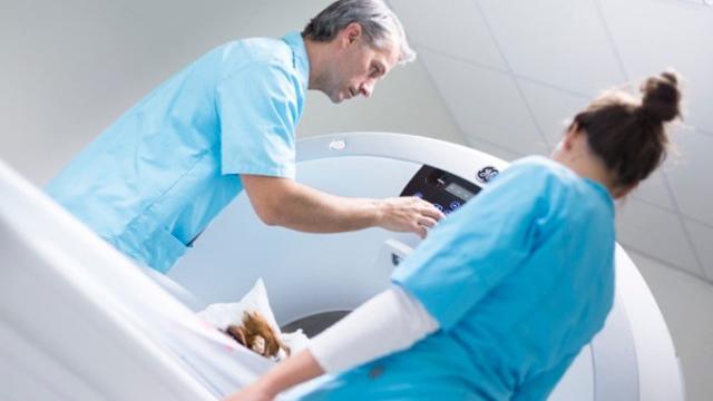 En lege justerer innstillinger på en CT-skanner mens en sykepleier assisterer pasienten.