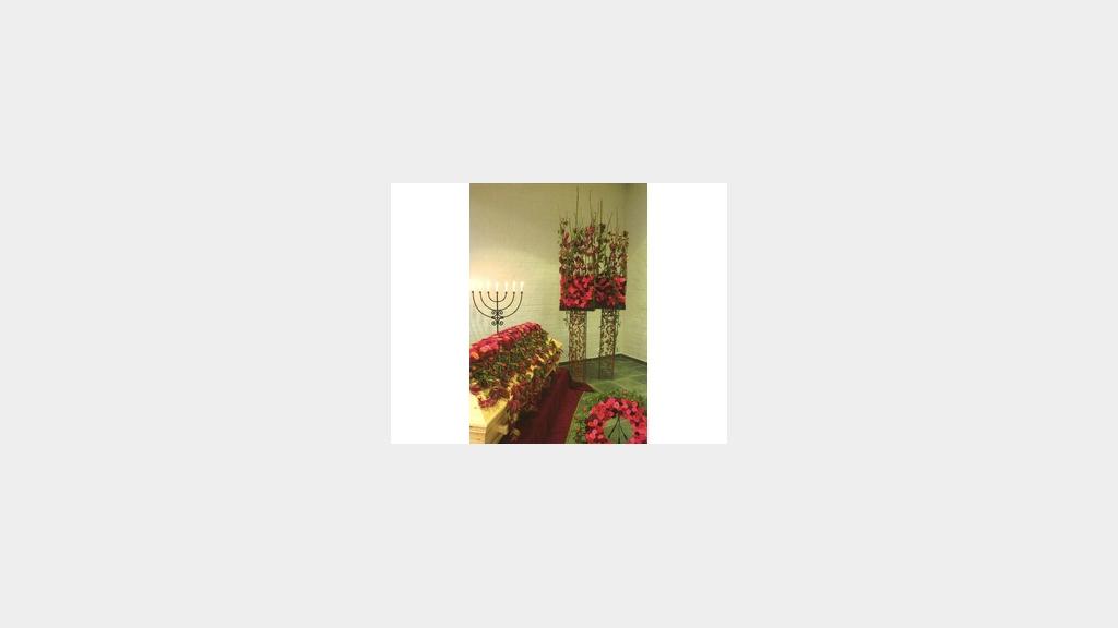Blomsterdekorasjoner i en stue med røde roser og grønne planter på et bord.